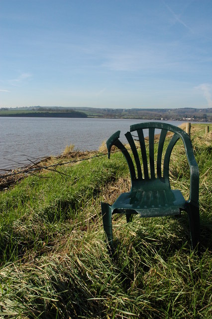 A photo of a damaged plastic chair on a grassy riverbank